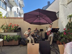 Dreiköpfige Band spielt im sonnigen Innenhof unter Sonnenschirm