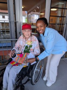 Pflegekraft mit Seniorin im Rollstuhl und Rose