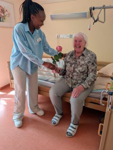Pflegekraft überreicht Seniorin eine Rose im Zimmer