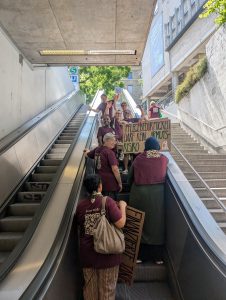 Demonstrierende mit Schild auf Rolltreppe am Bahnhof