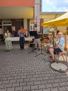 Bläserensemble spielt vor Café unter gelbem Sonnenschirm