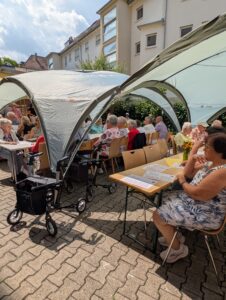 Seniorinnen und Senioren sitzen unter Pavillons bei Sommerfest